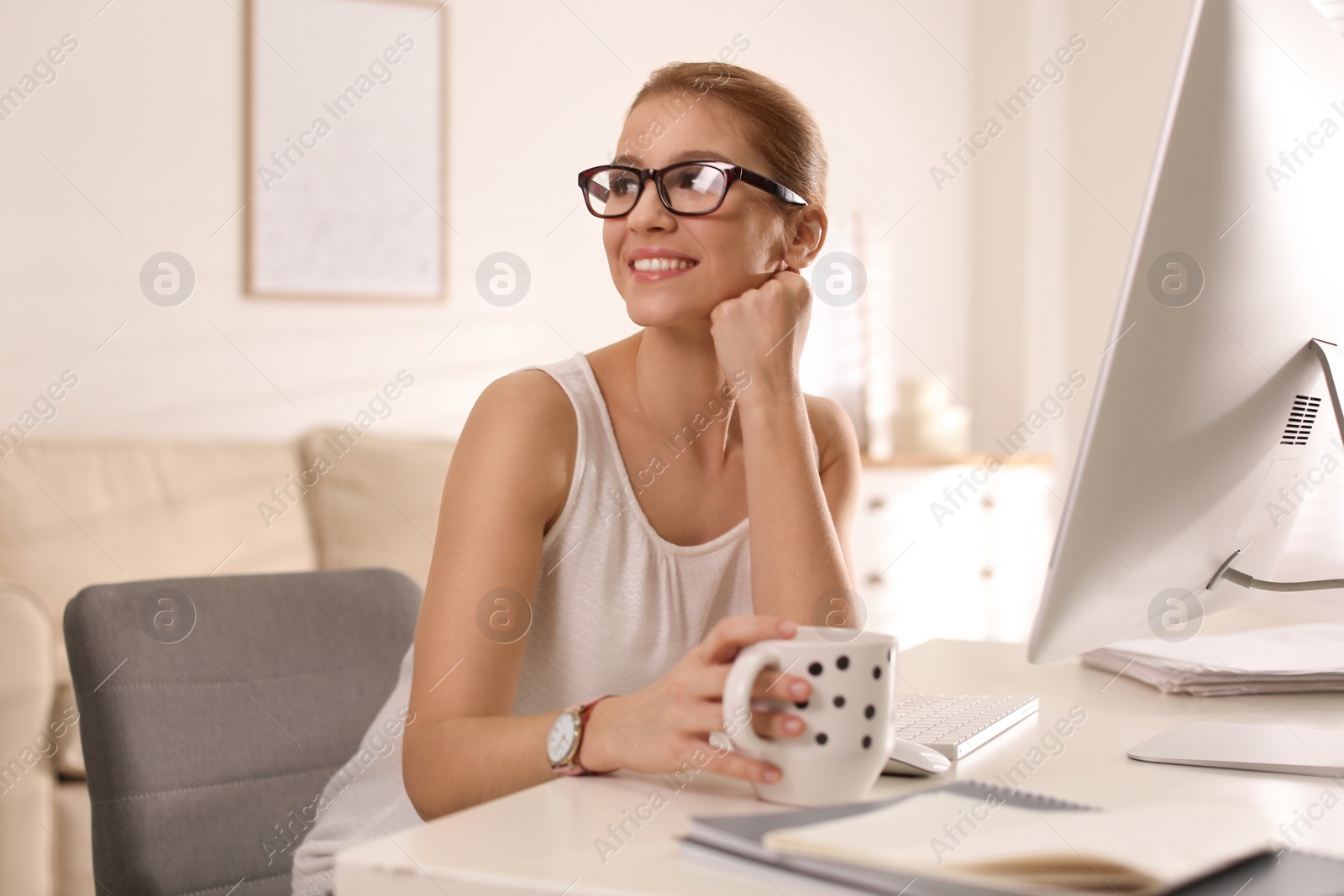 Photo of Young woman with cup of drink relaxing at table in office during break