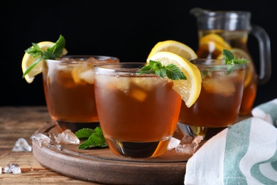 Photo of Delicious iced tea on wooden table against black background