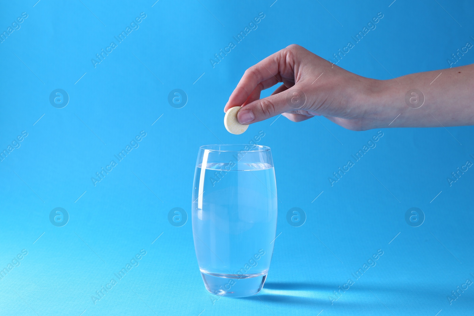 Photo of Woman putting effervescent pill into glass of water on light blue background, closeup