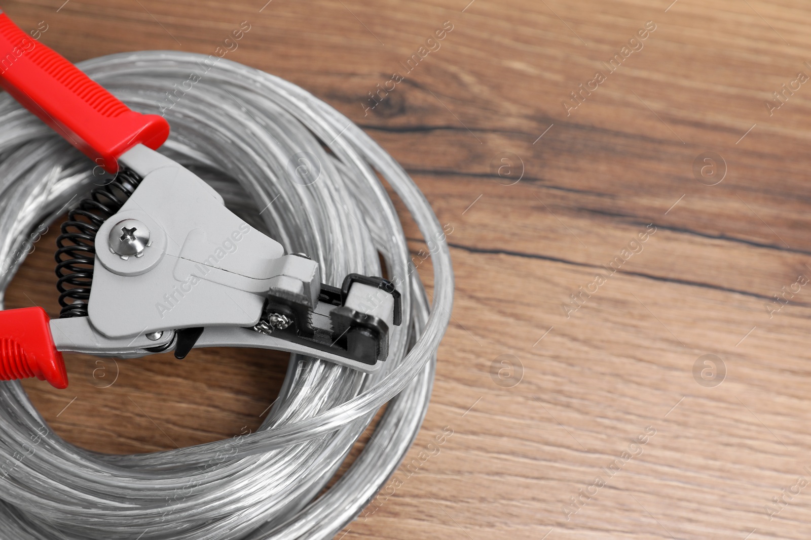 Photo of Cutters and cable with stripped wire on wooden table, closeup. Space for text