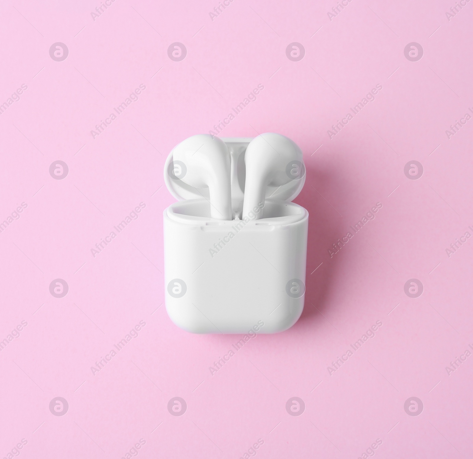 Photo of Modern wireless earphones in charging case on pink background, top view