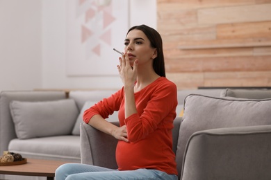 Young pregnant woman smoking cigarette at home