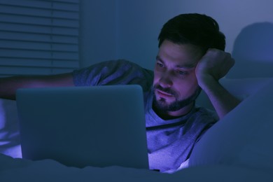 Photo of Man using laptop in bed at night. Internet addiction