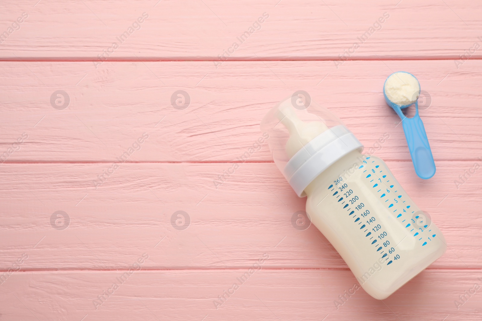 Photo of Feeding bottle with infant formula and powder on pink wooden table, flat lay. Space for text