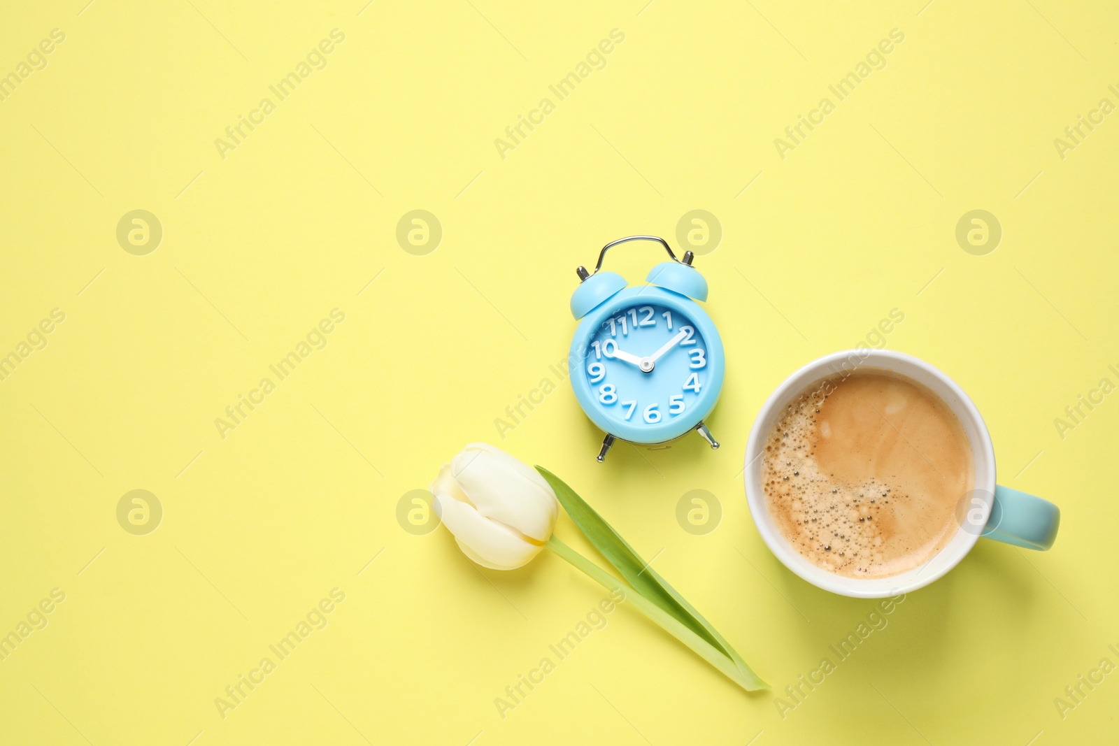 Photo of White tulip, alarm clock and coffee on yellow background, flat lay with space for text. Good morning