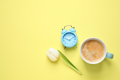 Photo of White tulip, alarm clock and coffee on yellow background, flat lay with space for text. Good morning