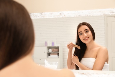 Photo of Beautiful young woman with hair comb near mirror in bathroom