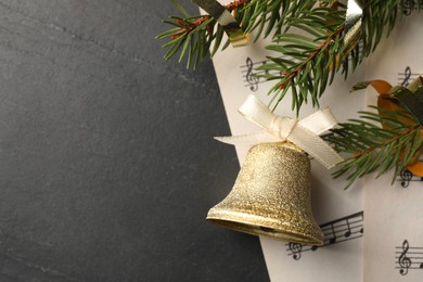 Golden shiny bell with white bow, fir branches and music sheets on grey table, top view and space for text. Christmas decoration