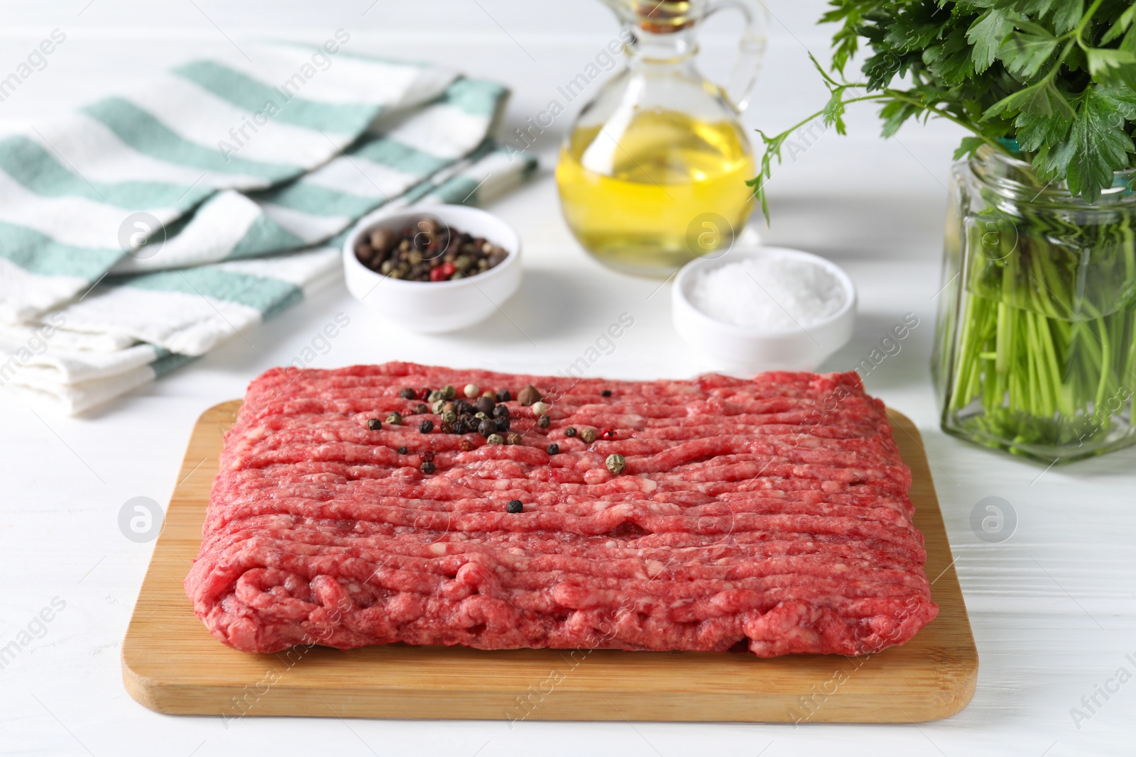 Photo of Raw ground meat, spices, oil and parsley on white wooden table