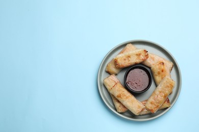 Photo of Fried spring rolls and sauce on light blue table, top view. Space for text