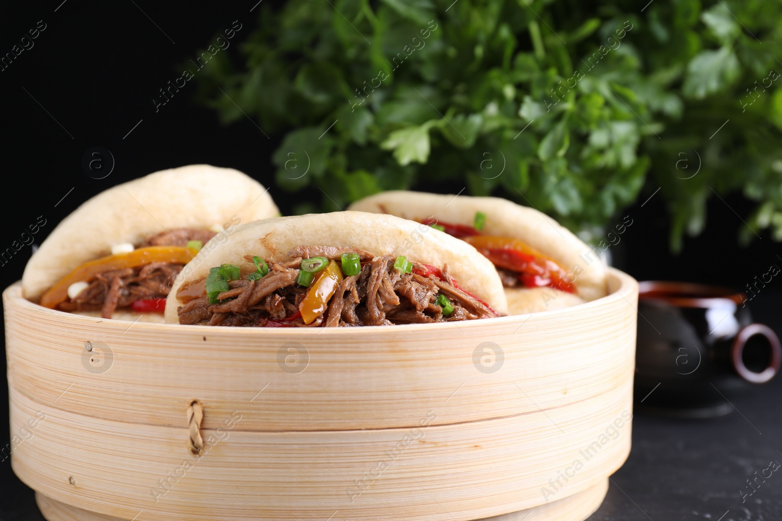 Photo of Delicious gua bao in bamboo steamer on black table, closeup