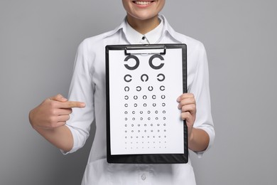 Photo of Ophthalmologist pointing at vision test chart on gray background, closeup