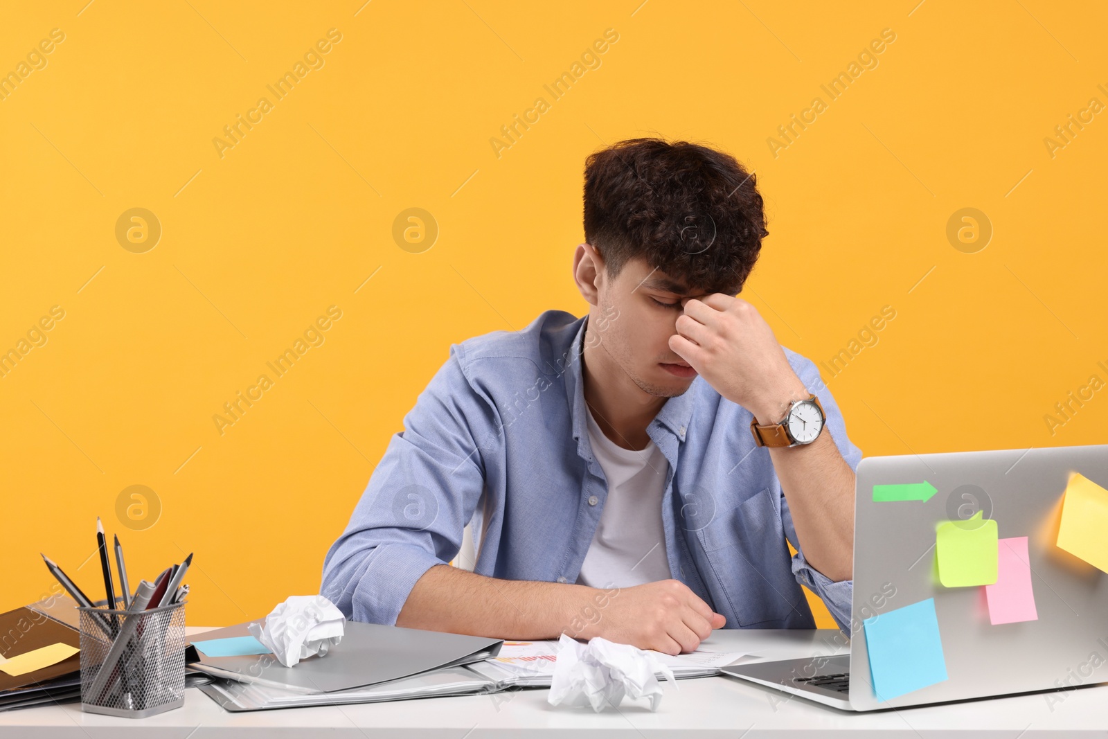 Photo of Tired young man working at white table on orange background. Deadline concept