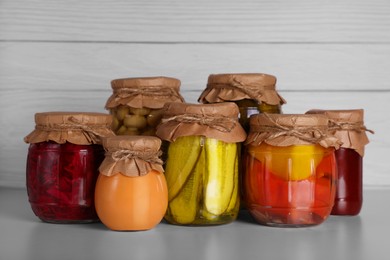 Photo of Many jars with different preserved vegetables and mushrooms on light grey table