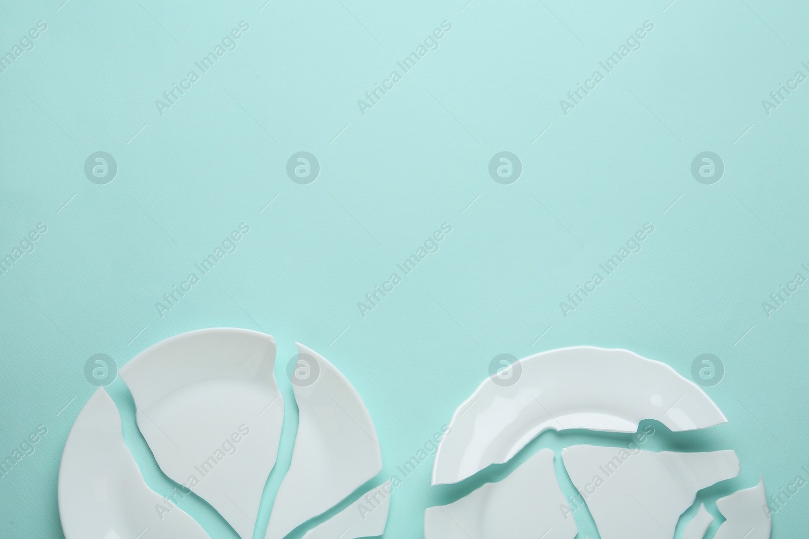 Photo of Two broken ceramic plates on light blue background, flat lay. Space for text