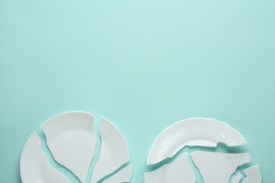 Photo of Two broken ceramic plates on light blue background, flat lay. Space for text