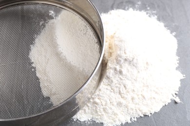 Metal sieve and flour on grey table, closeup