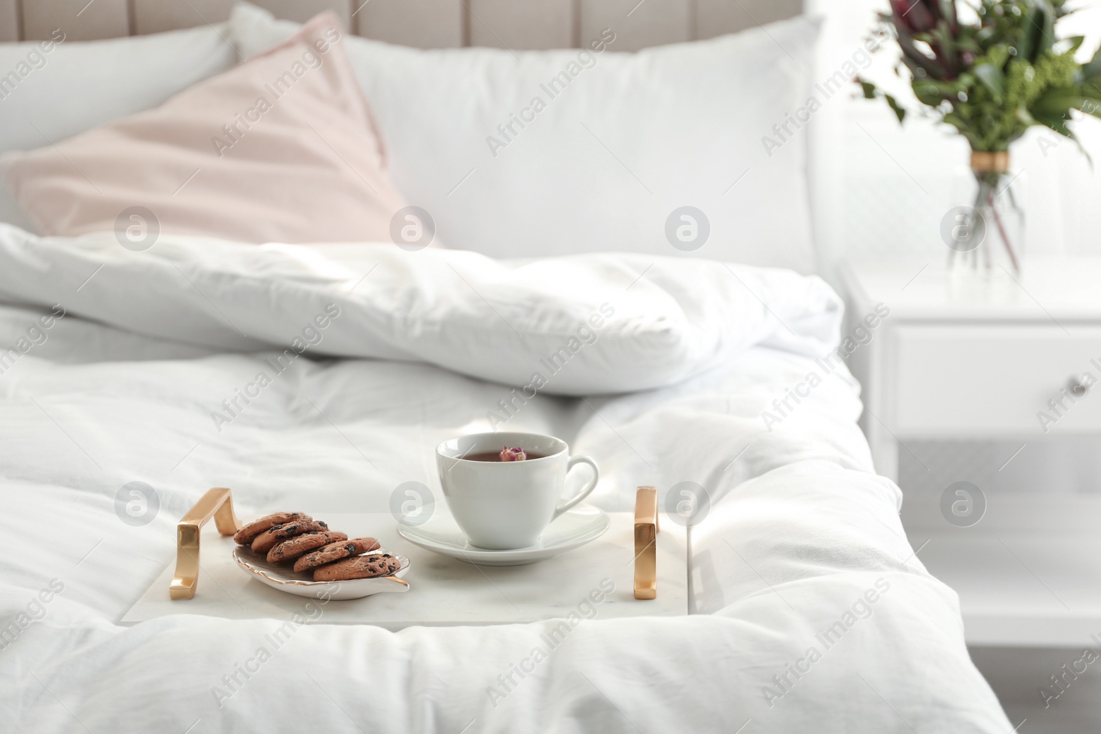 Photo of Cup of aromatic tea and cookies on soft blanket in bedroom