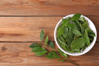 Photo of Aromatic fresh bay leaves and bowl on wooden table, flat lay. Space for text