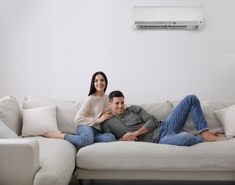 Happy couple resting under air conditioner on white wall at home