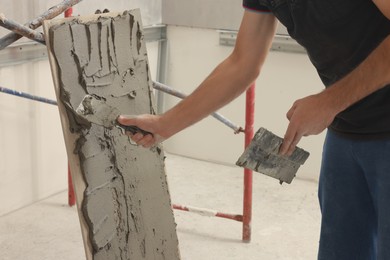 Photo of Worker spreading adhesive mix over tile with spatula, closeup