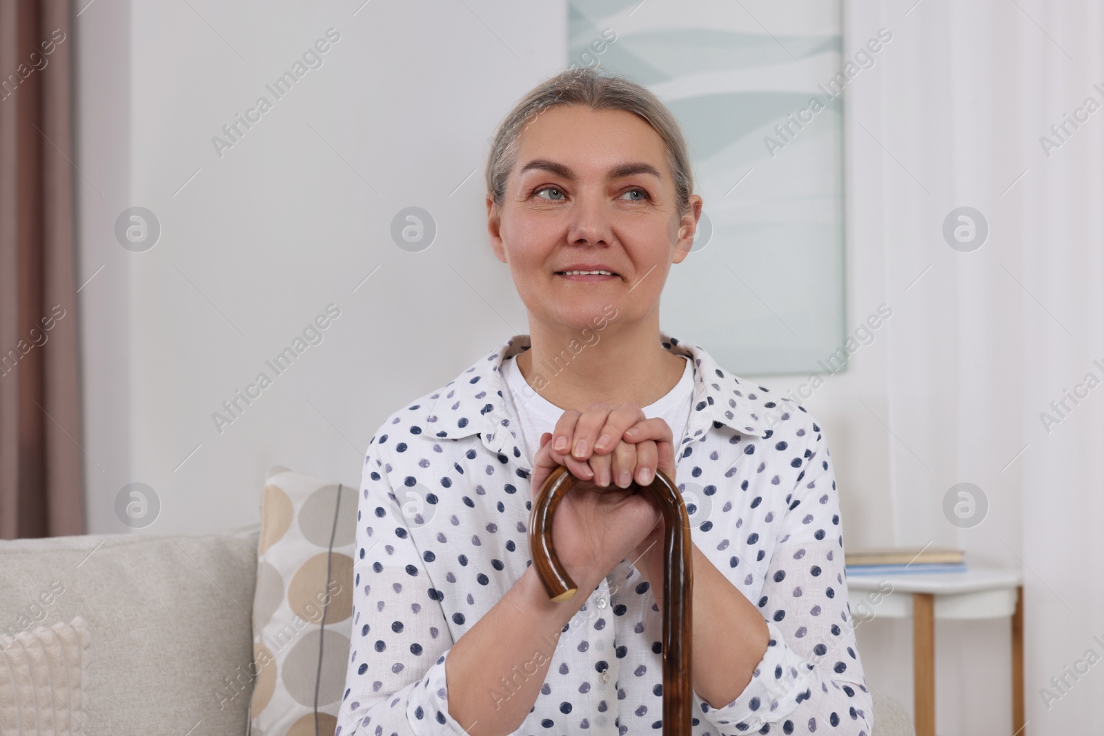 Photo of Senior woman with walking cane sitting on sofa at home