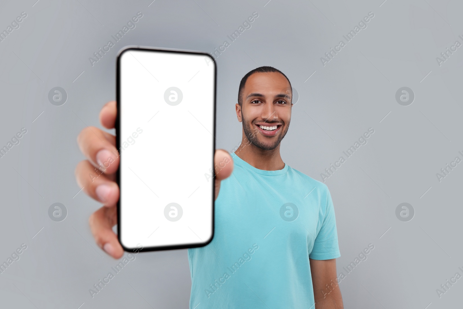 Photo of Young man showing smartphone in hand on light grey background