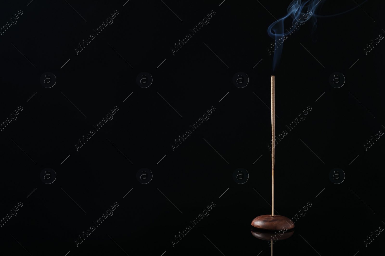 Photo of Incense stick smoldering in holder on black background. Space for text