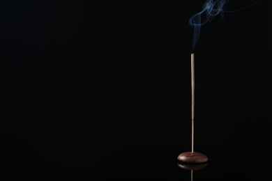 Photo of Incense stick smoldering in holder on black background. Space for text