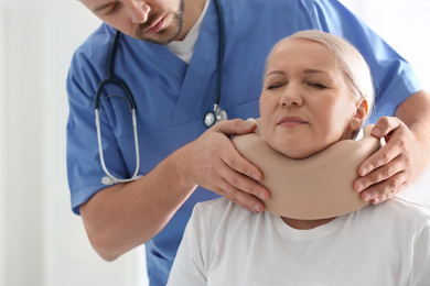 Photo of Orthopedist applying cervical collar onto patient's neck in clinic, closeup