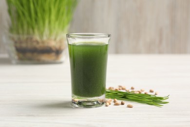 Photo of Wheat grass drink in shot glass, seeds and fresh green sprouts on white wooden table, closeup