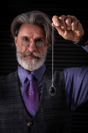 Photo of Psychotherapist with pendulum on black background. Hypnotherapy session