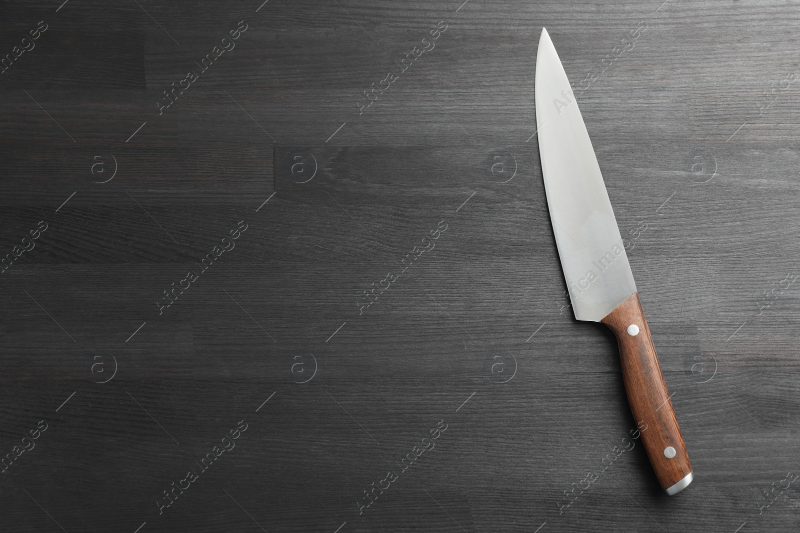 Photo of One sharp knife on black wooden table, top view. Space for text