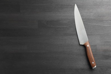 Photo of One sharp knife on black wooden table, top view. Space for text