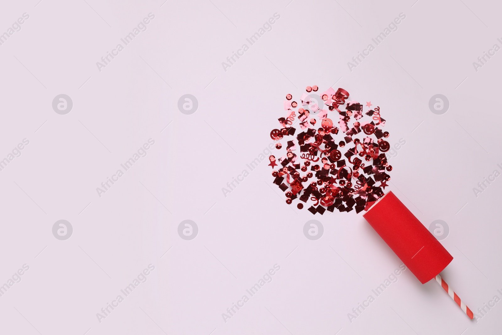 Photo of Shiny red confetti bursting out of party cracker on light background, top view. Space for text