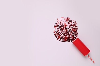 Photo of Shiny red confetti bursting out of party cracker on light background, top view. Space for text