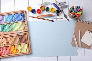 Photo of Blank sheet of paper, colorful chalk pastels and other drawing tools on white wooden table, flat lay. Modern artist's workplace