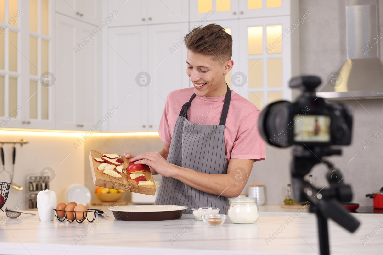 Photo of Smiling food blogger cooking while recording video in kitchen