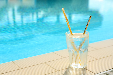 Glass of refreshing drink near swimming pool. Space for text