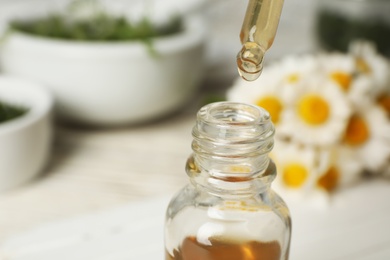 Pipette with essential oil over bottle on blurred background, closeup. Space for text