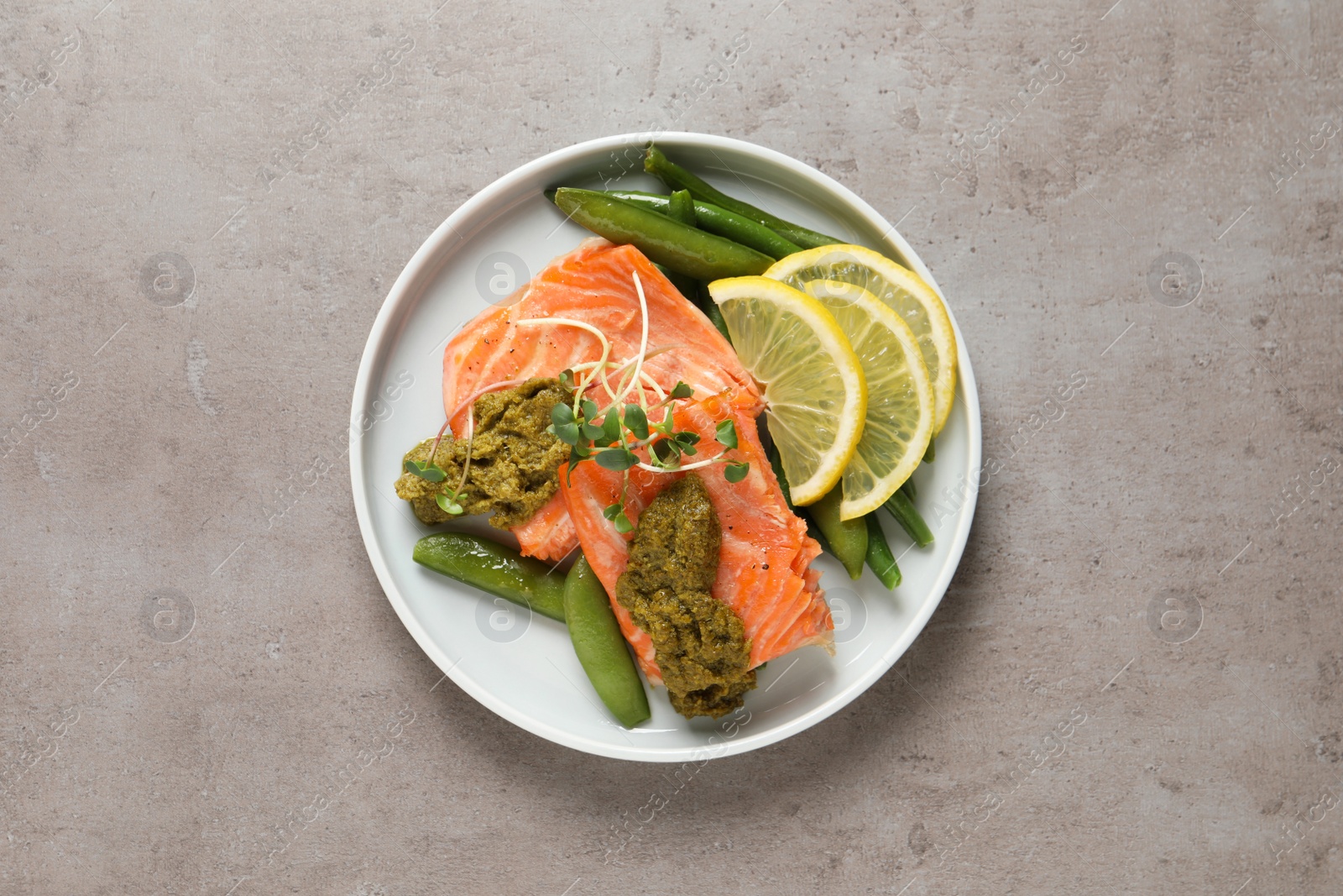 Photo of Tasty cooked salmon with pesto sauce on grey table, top view