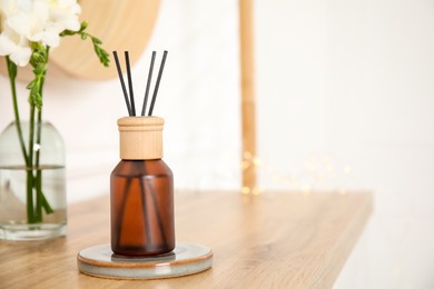 Photo of Reed diffuser and vase with bouquet on wooden table in room. Space for text