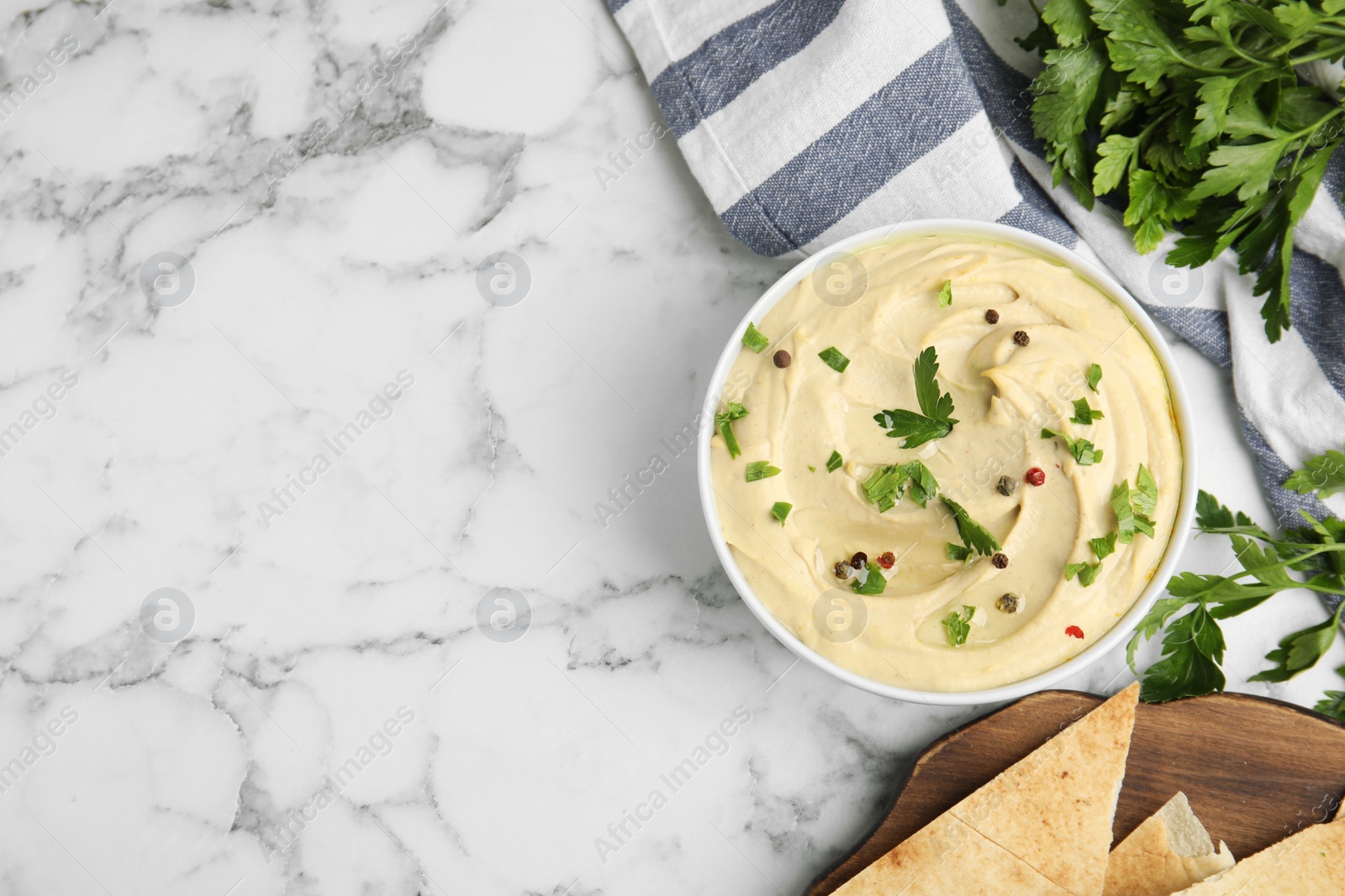 Photo of Delicious hummus with parsley and pita chips on white marble table, flat lay. Space for text