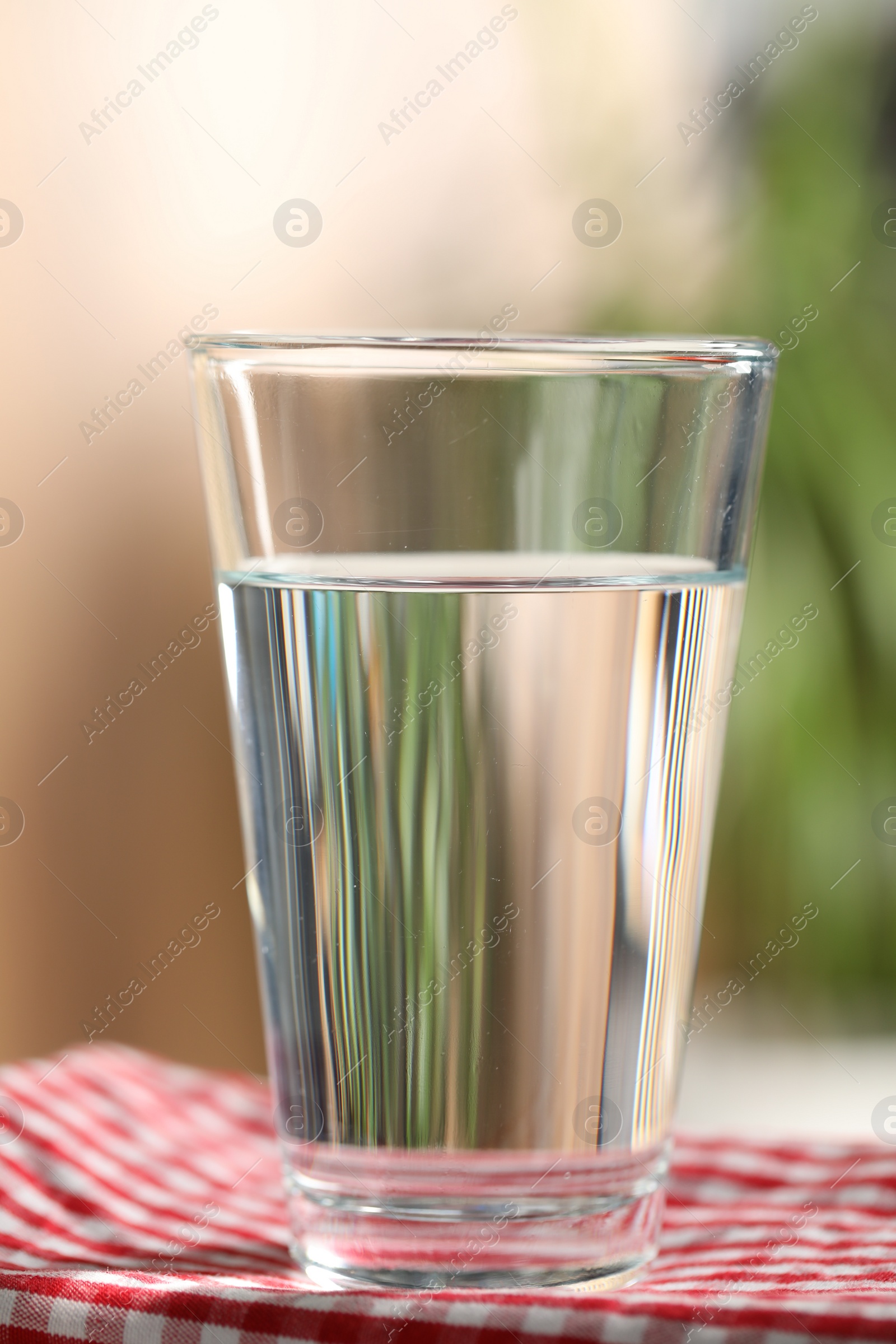 Photo of Glass of pure water on red kitchen towel against blurred background, closeup