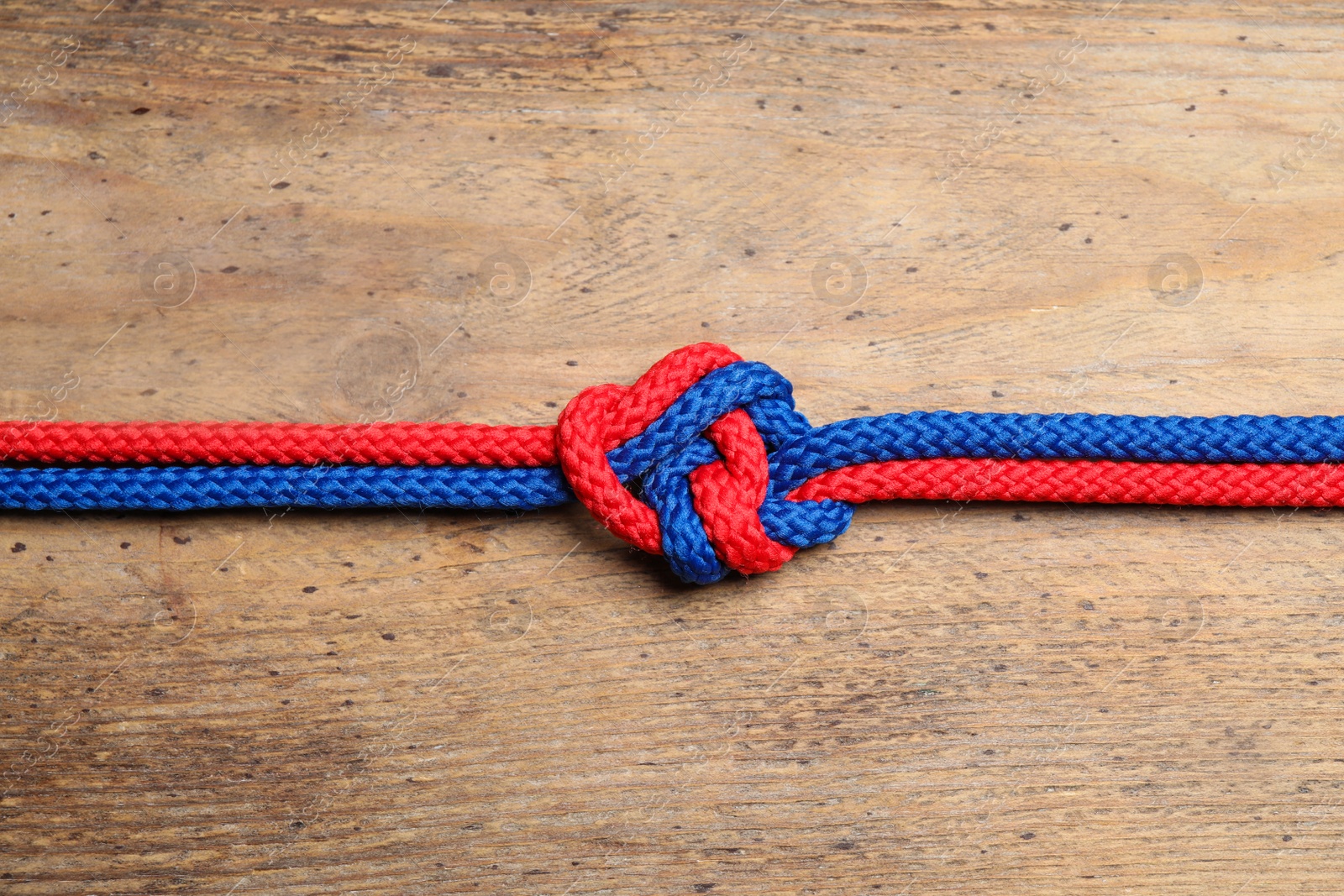 Photo of Colorful ropes tied together on wooden background, top view. Unity concept
