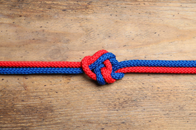 Colorful ropes tied together on wooden background, top view. Unity concept