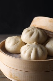 Photo of Delicious bao buns (baozi) in bamboo steamer on table against black background, closeup