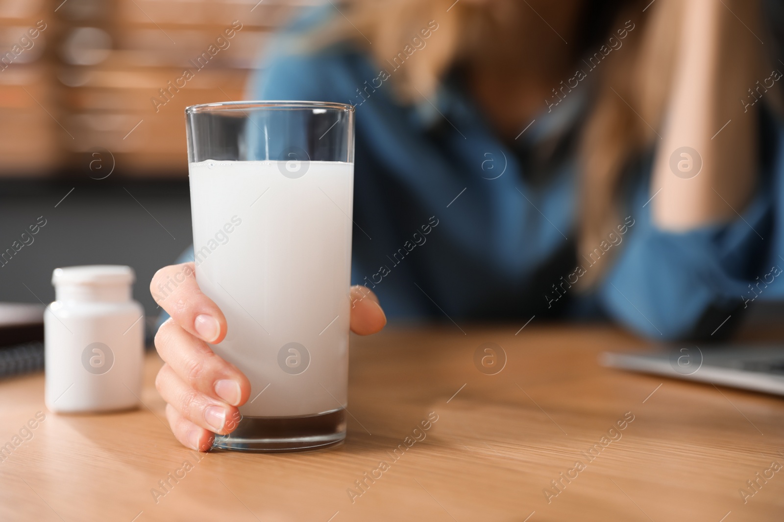 Photo of Woman taking medicine for hangover in office, focus on hand with glass