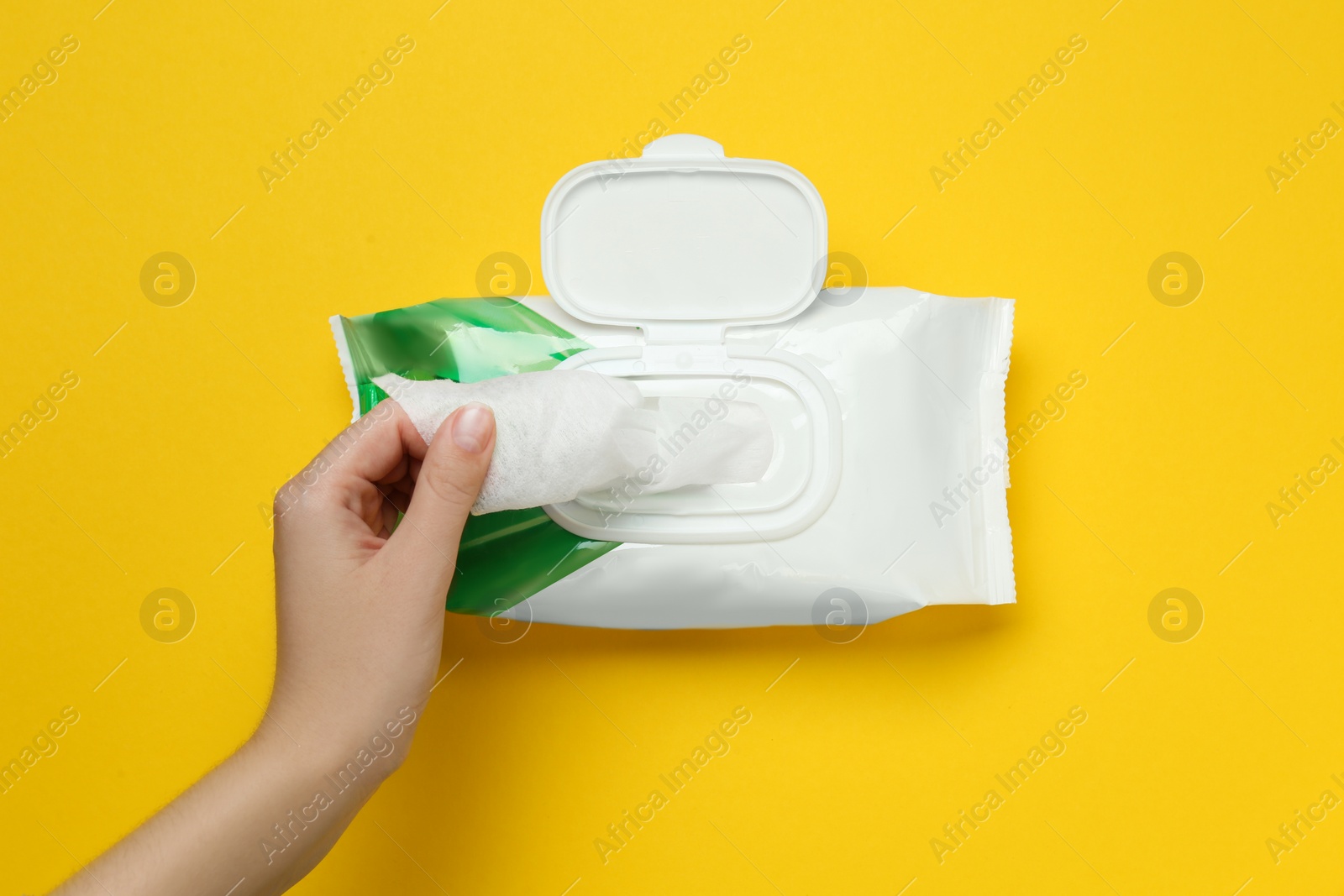 Image of Woman taking wet wipe from pack on yellow background, top view