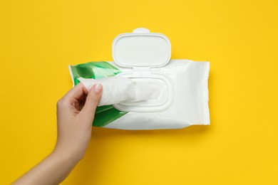 Woman taking wet wipe from pack on yellow background, top view